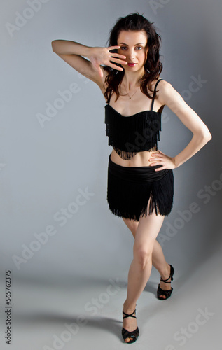 Beautiful young woman with evening make-up and hairdo dancing in elegant black dress with passion. Studio portrait on a gray background. Dancing, tango style.