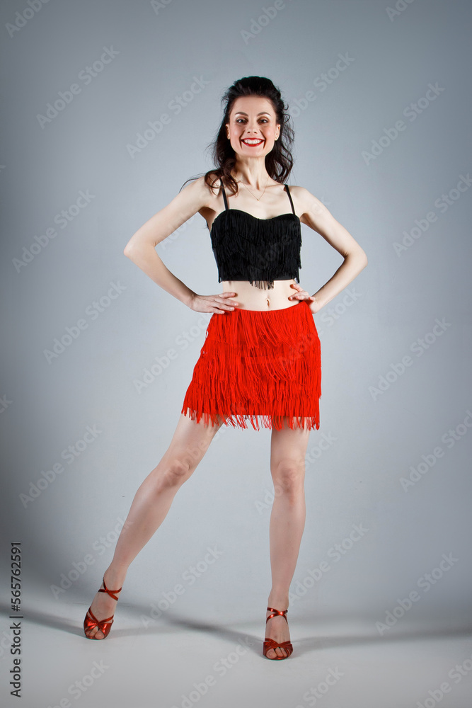 An elegant dancer performs a Latin American dance in an elegant red dress with sparkling jewelry. Fashion and beauty. Ballet show. Studio portrait. An elegant dancer performs a Latin American dance in an elegant red dress with sparkling jewelry. Fashion and beauty. Ballet show. Studio portrait.
