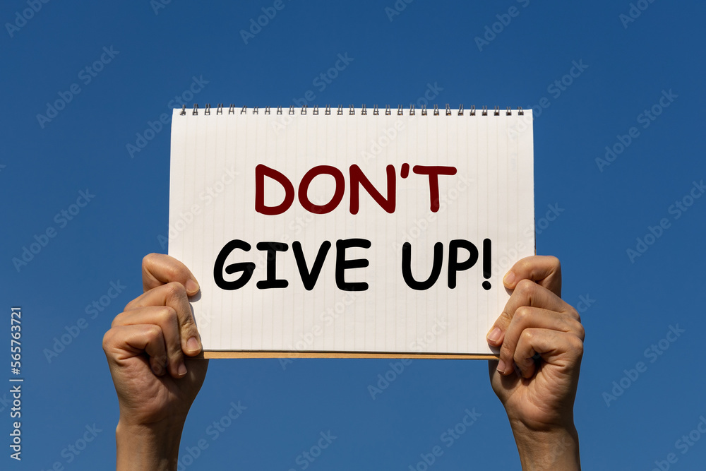 Don't give up text on notebook paper that is held by 2 hands with blue sky as background. This can be used any business purpose on any media such as website, advertisement, etc.