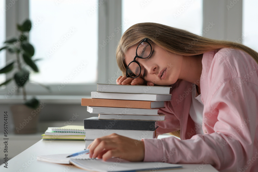 Young tired woman sleeping near books at white table in room Young tired woman sleeping near books at white table in room