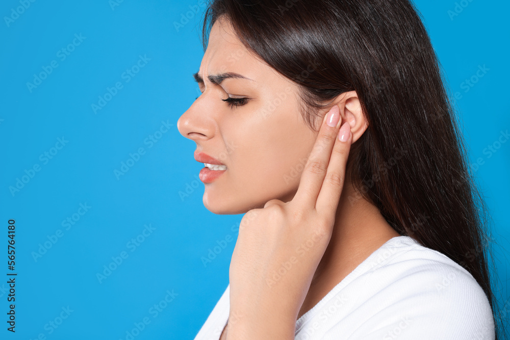 Young woman suffering from ear pain on light blue background, closeup. Space for text Young woman suffering from ear pain on light blue background, closeup. Space for text