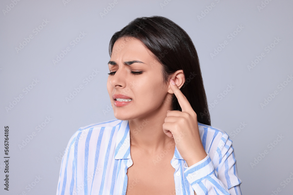 Young woman suffering from ear pain on light grey background Young woman suffering from ear pain on light grey background