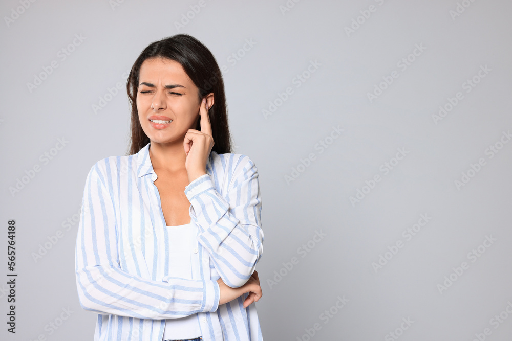 Young woman suffering from ear pain on light grey background, space for text Young woman suffering from ear pain on light grey background, space for text