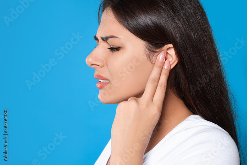 Young woman suffering from ear pain on light blue background, closeup. Space for text