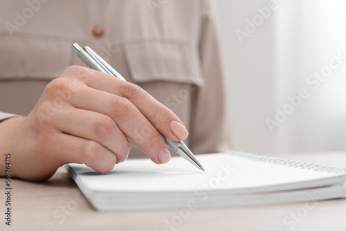 Woman writing in notebook at wooden table, closeup