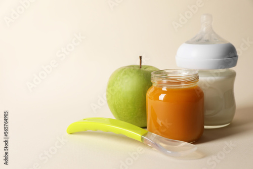Healthy baby food in jar, bottle of milk, apple and spoon on beige background. Space for text