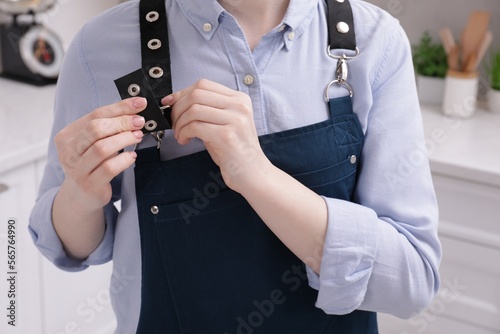 Woman putting on apron in kitchen , closeup