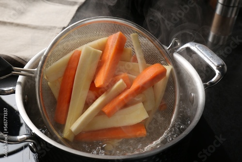 Putting cut parsnips and carrots into pot with boiling water in kitchen, closeup