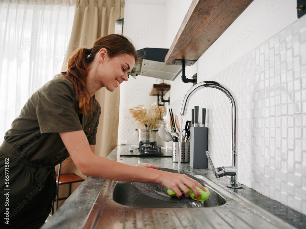 Woman smiling with teeth hands without gloves washes dishes with a dishwashing sponge, household chores, no dishwasher, high water consumption. Stylish kitchen design Woman smiling with teeth hands without gloves washes dishes with a dishwashing sponge, household chores, no dishwasher, high water consumption. Stylish kitchen design
