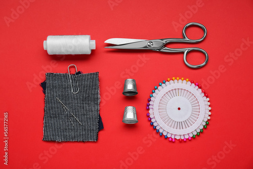 Flat lay composition with thimbles and different sewing tools on red background