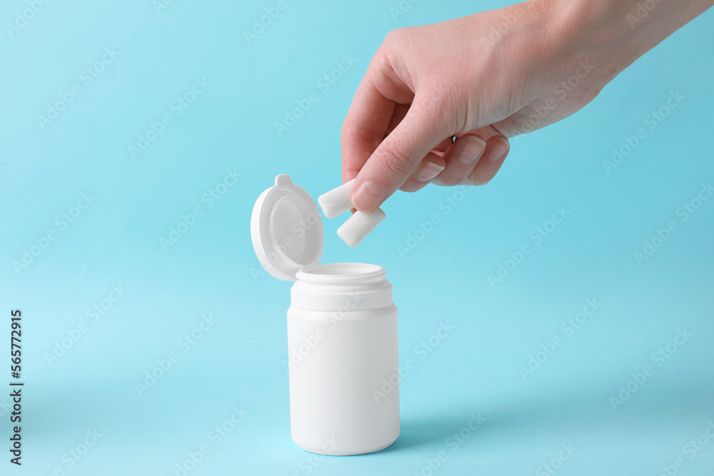Woman taking chewing gums from jar on light blue background, closeup