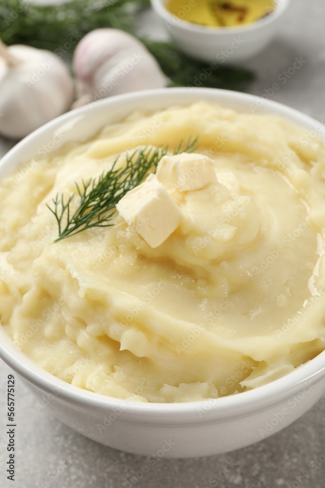 Bowl of delicious mashed potato with dill and butter on light grey table, closeup