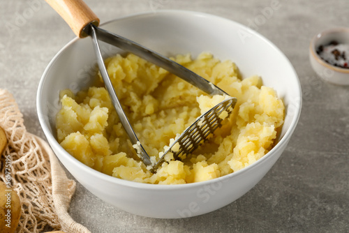 Bowl with delicious mashed potato and masher on light grey table, closeup photo