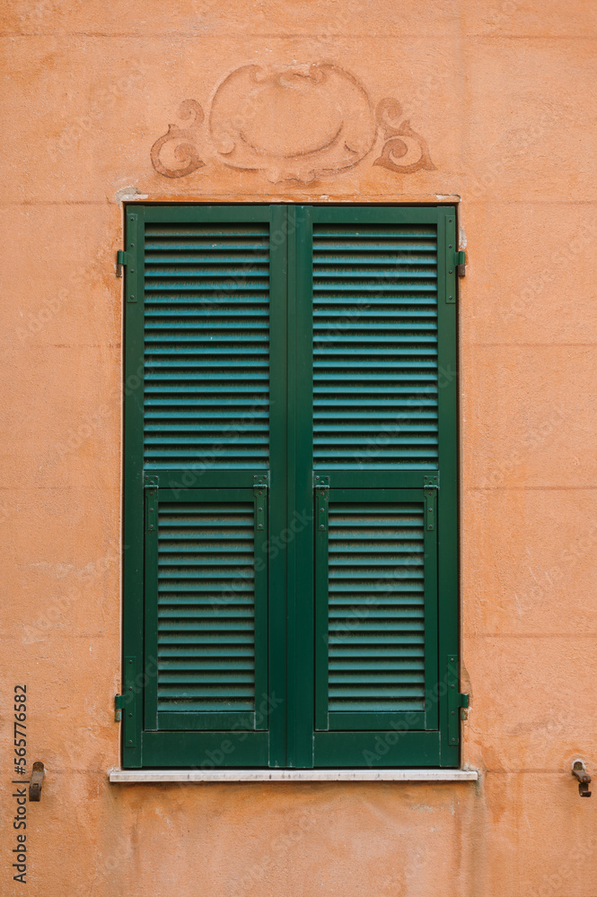 Orange wall with green window on street in Liguria Italy