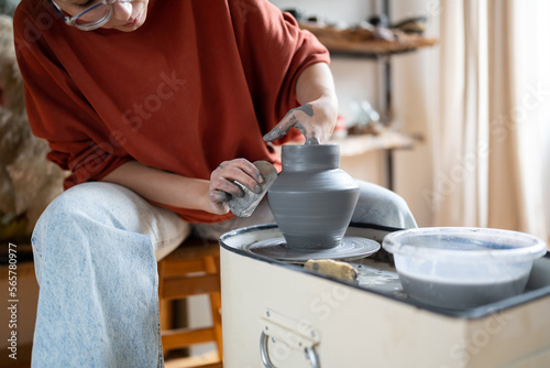 Attentive woman sits in pottery workshop and diligently does what she loves, which brings income and pleasure. Female makes aesthetic items for home with own hands. Working with clay for mental health © DimaBerlin