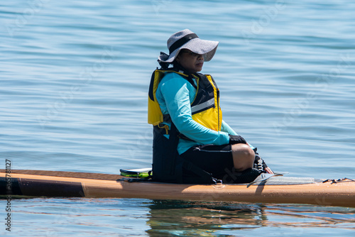 Woman sail on a SUP boards with special seating chair and wet suit and life jacket for paddling. Stand up paddle boarding active recreation leisure and sport at lake water. Active vacation.