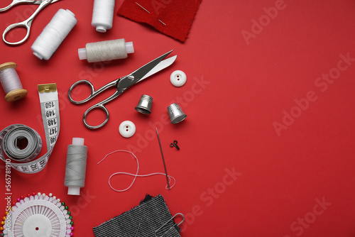 Flat lay composition with thimbles and different sewing tools on red background. Space for text
