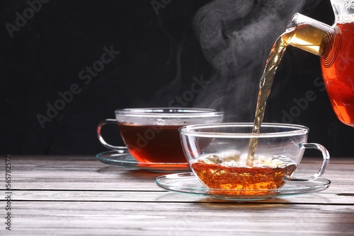 Pouring tea into glass cup on wooden table against black background, space for text