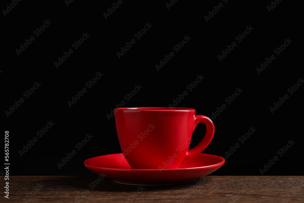 Red cup on wooden table against black background Red cup on wooden table against black background