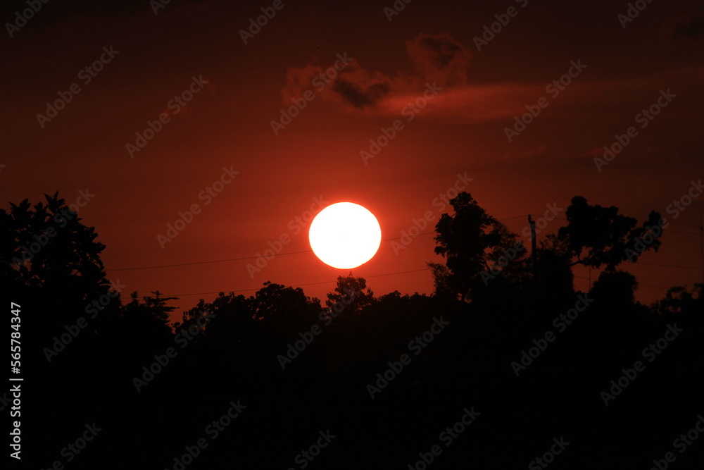 photo of the sun setting in a corner of the village with the silhouette of trees