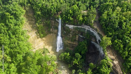 Cliff in middle of green forest and small beautiful picturesque waterfall. Precipitous waterfall that surrounds greenery flooded with bright morning sunshine. Drone view of waterfall in Malaysia.