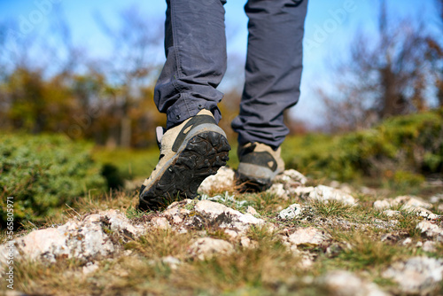 Legs of a hiker in trekking boots walking in the mountains closeup shot. Feet of walking tourist wearing trekking shoes on a rocky road captured from behind. Hiking male wearing pants and boots walk