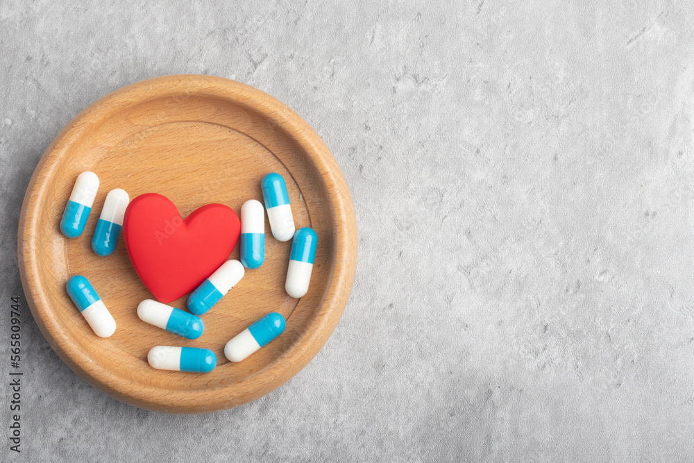 Medicine capsule and heart in wooden cup on gray background. Copy space. Medical treatment concept. Medicine capsule and heart in wooden cup on gray background. Copy space. Medical treatment concept.