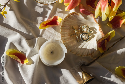 Morning still life with candles, vintage bell extinguishing, tulip petals, jewelry earrings, pearl in seashell. Top view