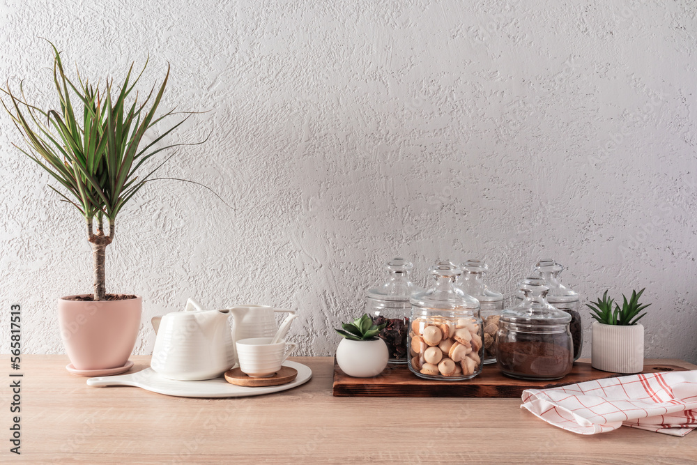 Fototapeta premium kitchen interior , background. glass jars with dry tea, biscuits, coffee beans, white ceramic teapot and cups. Plants. front view.