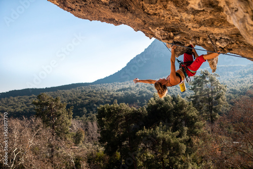 A young rock climber on an overhanging cliff. The climber climbs the rock. The girl is engaged in sports climbing.