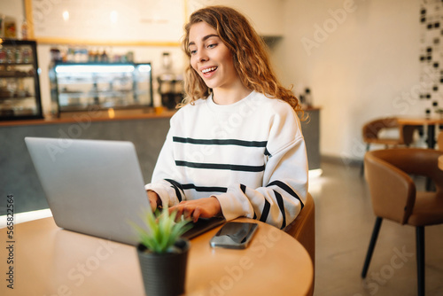 Woman sitting at her desk in cafe, typing text message using smart phone while working. Freelance, online course, remote work and lifestyle concept. 