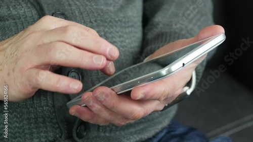 An old man uses a tablet while sitting on a sofa in the office. Modern technologies for the elderly.