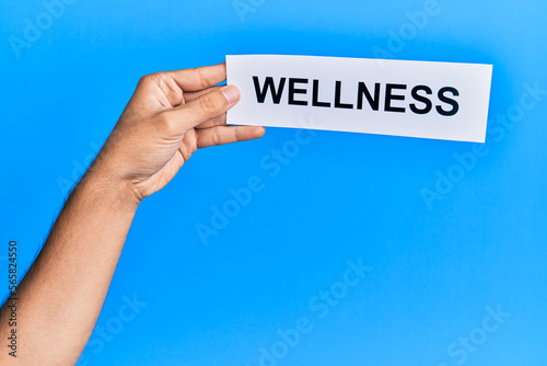 Hand of caucasian man holding paper with wellness word over isolated blue background