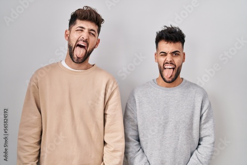 Young homosexual couple standing over white background sticking tongue out happy with funny expression. emotion concept.
