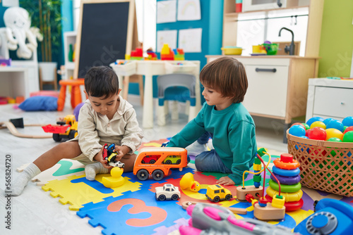 Two kids playing with cars toy sitting on floor at kindergarten