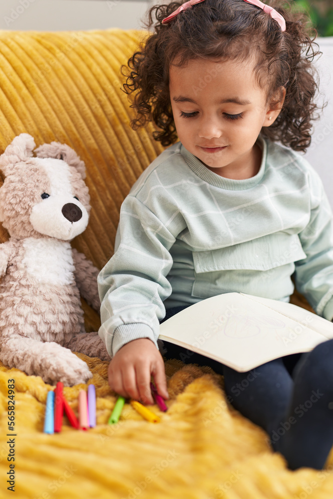 Adorable hispanic girl drawing on notebook sitting on sofa at home Adorable hispanic girl drawing on notebook sitting on sofa at home
