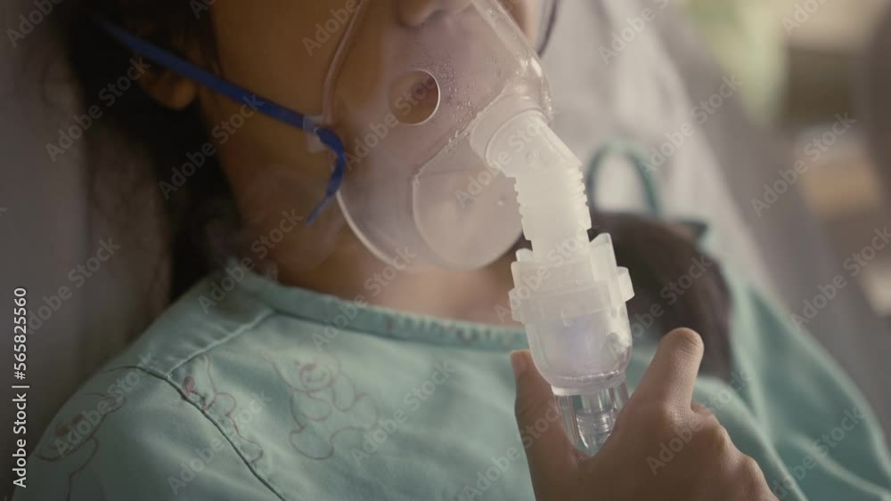 Asian girl having an oxygen mask and breathing through a nebulizer at the hospital.