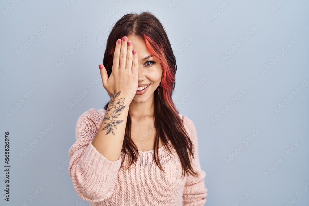 Young caucasian woman wearing pink sweater over isolated background covering one eye with hand, confident smile on face and surprise emotion. Young caucasian woman wearing pink sweater over isolated background covering one eye with hand, confident smile on face and surprise emotion.