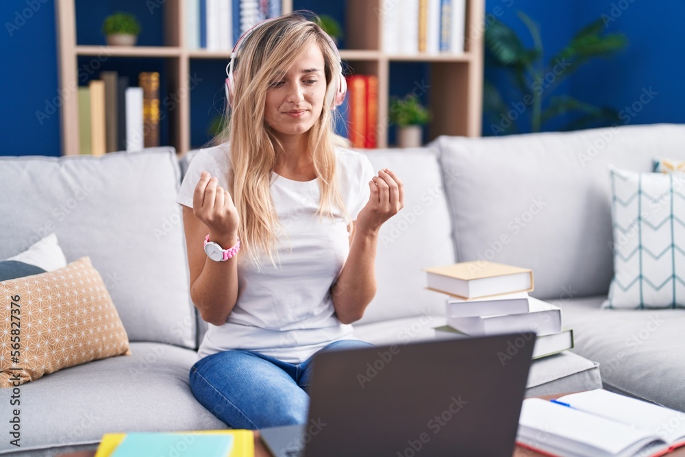 Young blonde woman studying using computer laptop at home doing money gesture with hands, asking for salary payment, millionaire business Young blonde woman studying using computer laptop at home doing money gesture with hands, asking for salary payment, millionaire business