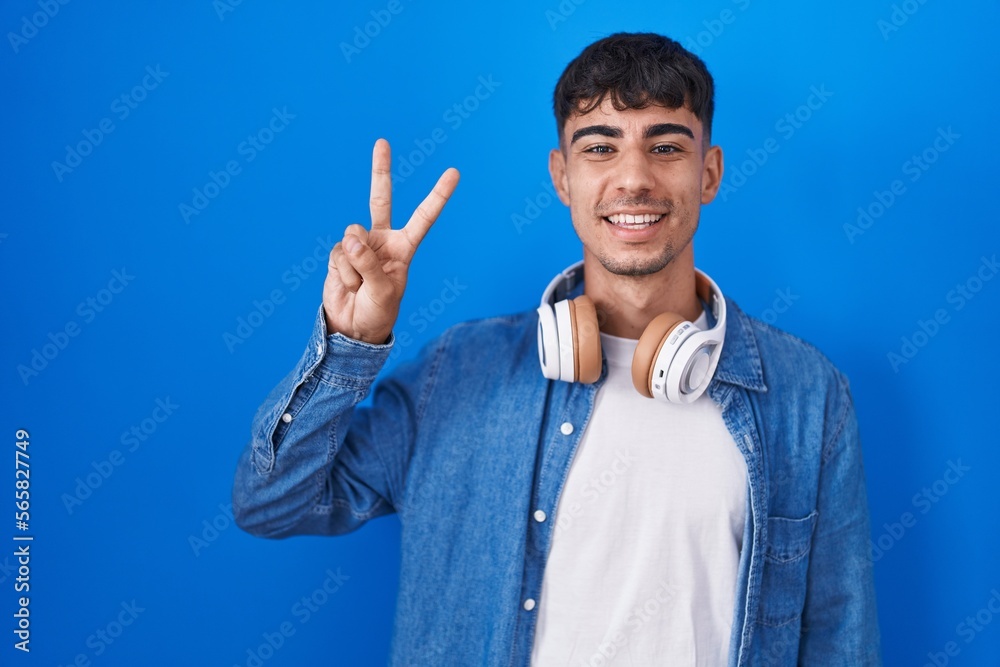Young hispanic man standing over blue background showing and pointing up with fingers number two while smiling confident and happy. Young hispanic man standing over blue background showing and pointing up with fingers number two while smiling confident and happy.