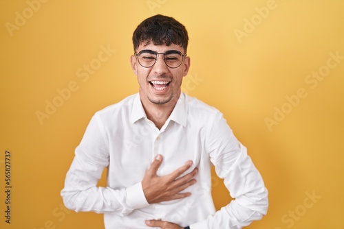 Young hispanic man standing over yellow background smiling and laughing hard out loud because funny crazy joke with hands on body.