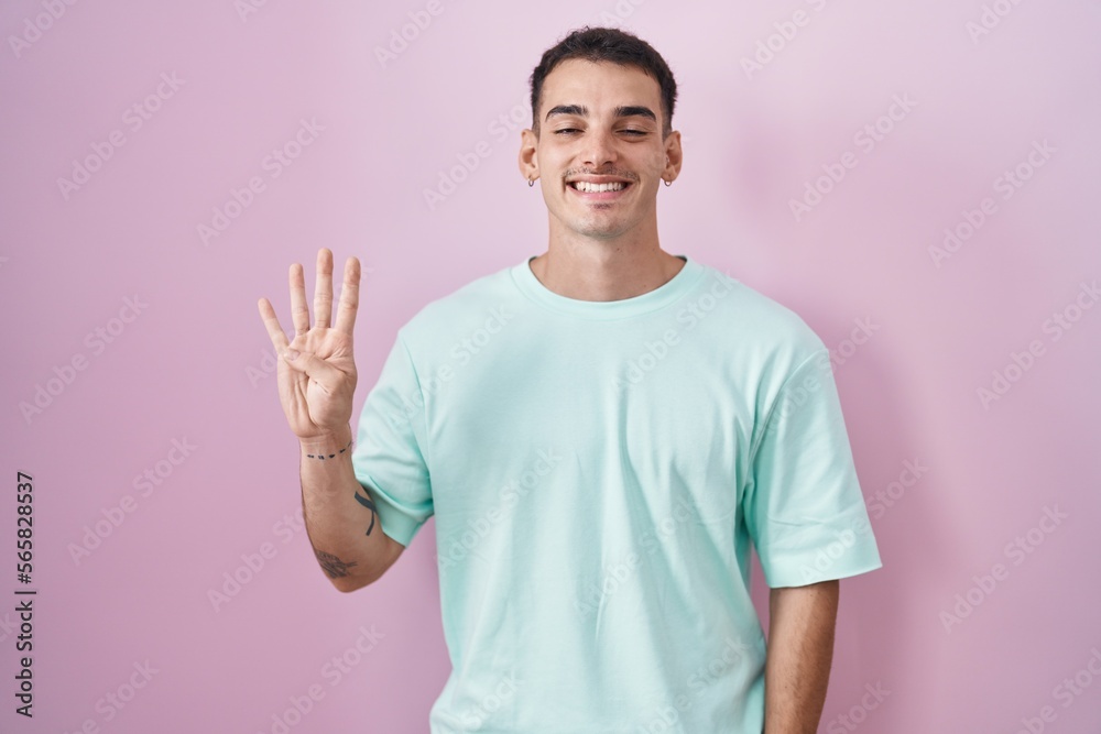 Handsome hispanic man standing over pink background showing and pointing up with fingers number four while smiling confident and happy.