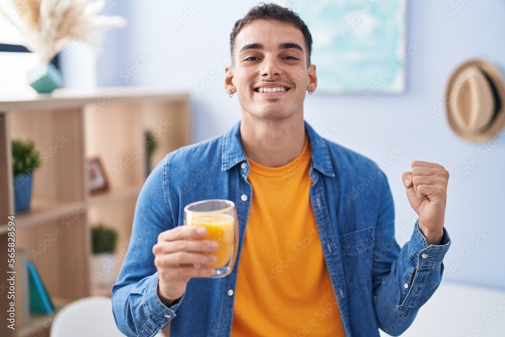 Handsome hispanic man drinking glass of orange juice screaming proud, celebrating victory and success very excited with raised arms Handsome hispanic man drinking glass of orange juice screaming proud, celebrating victory and success very excited with raised arms