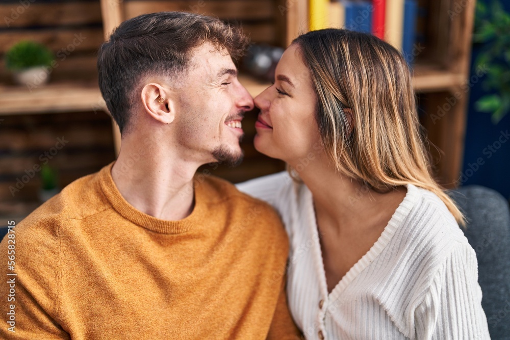 Naklejka premium Young man and woman couple hugging each other sitting on sofa at home