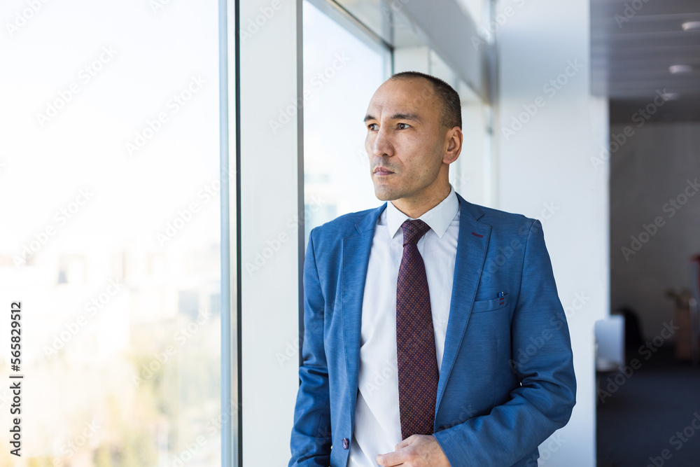 Portrait of a business young successful man in a modern office standing by the window against the backdrop of the city Portrait of a business young successful man in a modern office standing by the window against the backdrop of the city