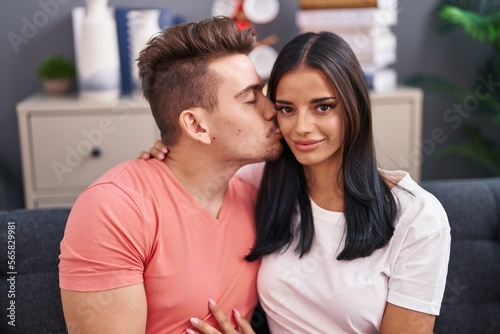 Man and woman couple hugging each other and kissing sitting on sofa at home