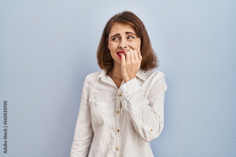 Young beautiful woman standing casual over blue background looking stressed and nervous with hands on mouth biting nails. anxiety problem. Young beautiful woman standing casual over blue background looking stressed and nervous with hands on mouth biting nails. anxiety problem.