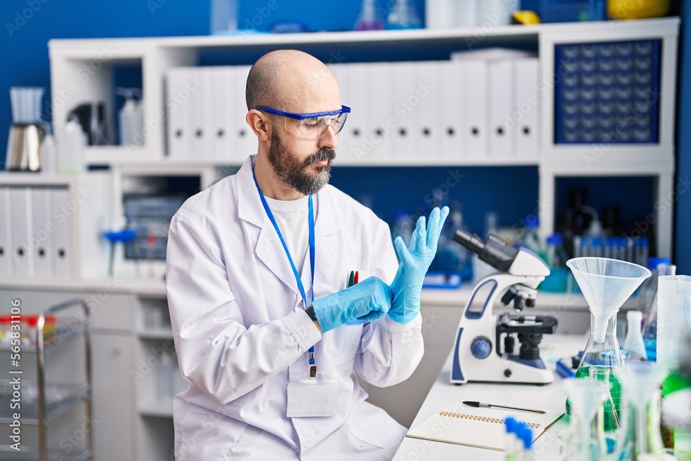 Young bald man scientist wearing gloves at laboratory