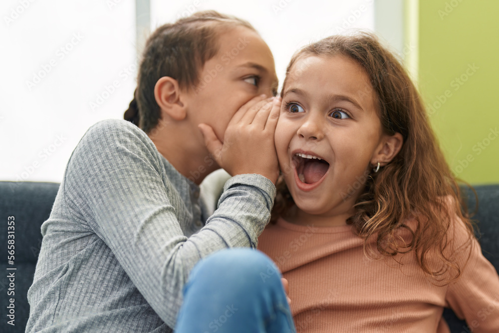 Two kids telling secret sitting on sofa at home Two kids telling secret sitting on sofa at home