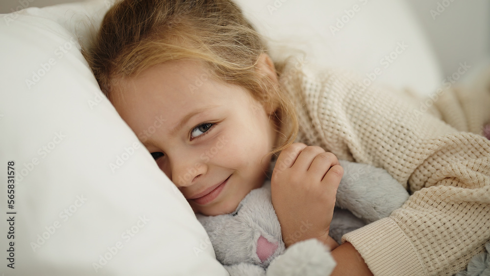 Adorable blonde girl hugging rabbit doll lying on bed at bedroom Adorable blonde girl hugging rabbit doll lying on bed at bedroom